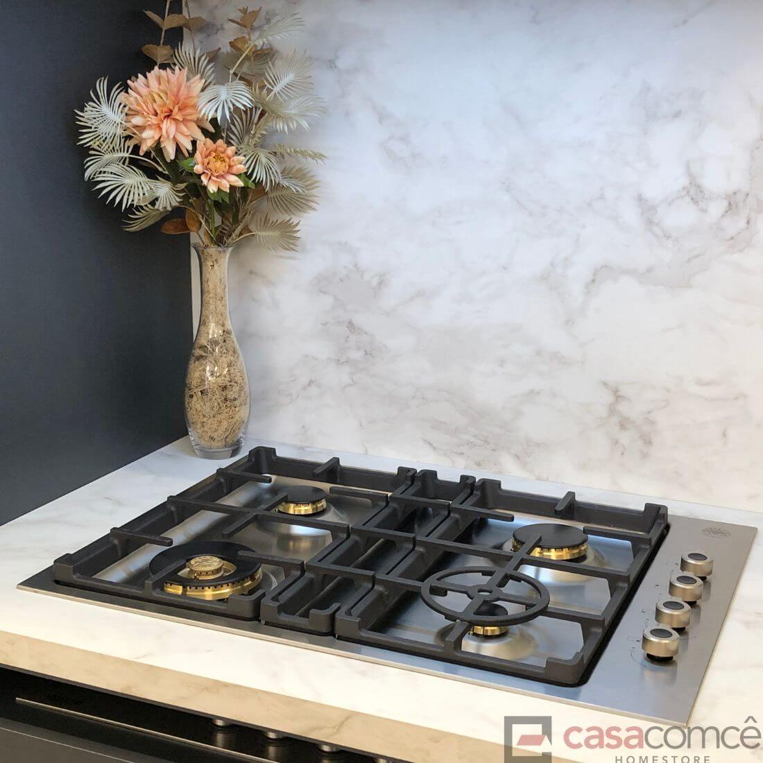 Cooktop Bertazzoni Profissional a gás 4 bocas em inox sobre bancada de mármore com flores decorativas.