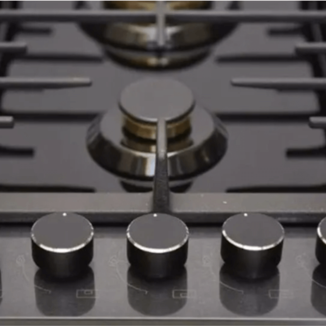 Close-up of Cuisinart Arkton gas cooktop controls with black knobs on tempered glass surface.