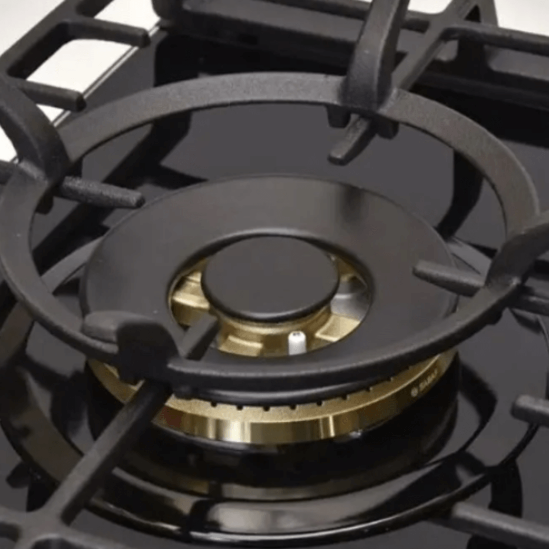 Close-up of a gas burner on a black tempered glass cooktop with cast iron grates.