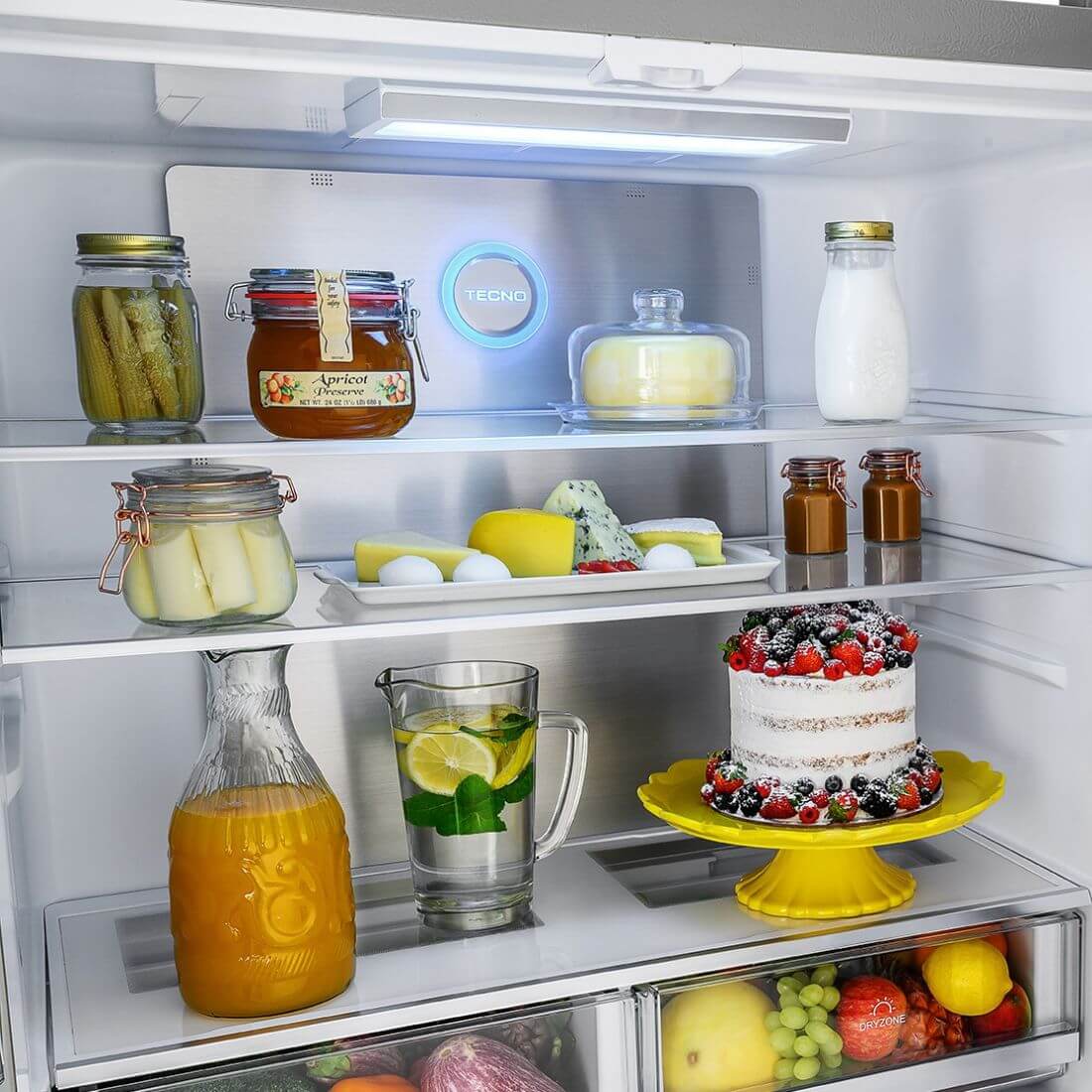 Interior do Refrigerador Tecno Professional com alimentos organizados, incluindo bolos e bebidas, iluminado por LED.
