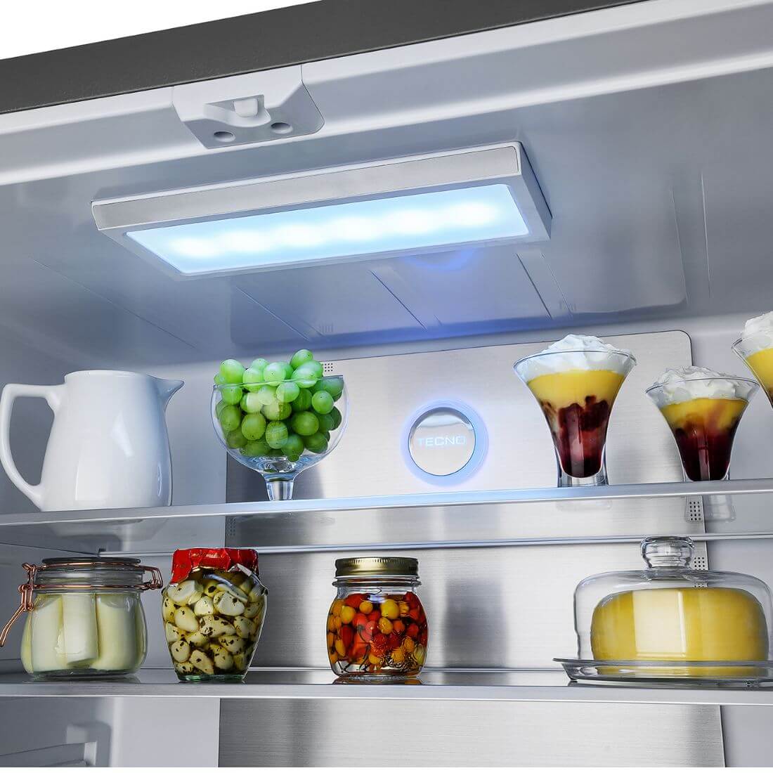 Interior iluminado de refrigerador Tecno Professional com frutas, sobremesas e objetos organizados.