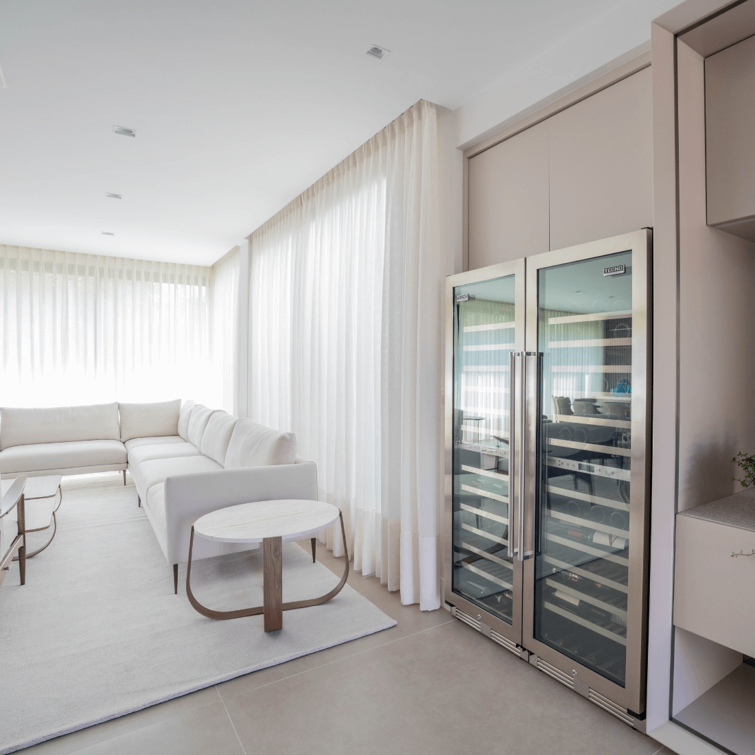 Adega de vinhos Tecno Professional em ambiente moderno, ao lado de sofá e mesa de centro.