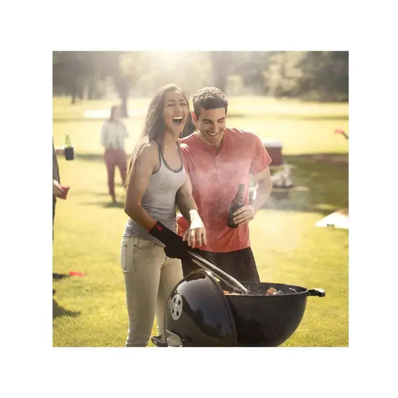Casal se divertindo ao utilizar a churrasqueira a carvão Weber Original Kettle em um dia ensolarado.