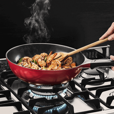 Panela vermelha com camarões sendo cozinhados em fogão a gás, com vapor saindo e colher de madeira.