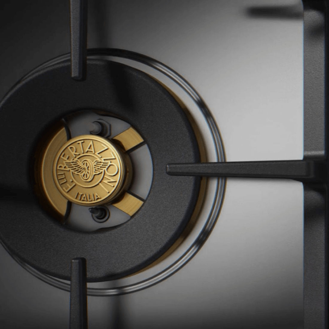 Detale do queimador a gás do cooktop Bertazzoni, com logotipo em dourado e trempes robustas.