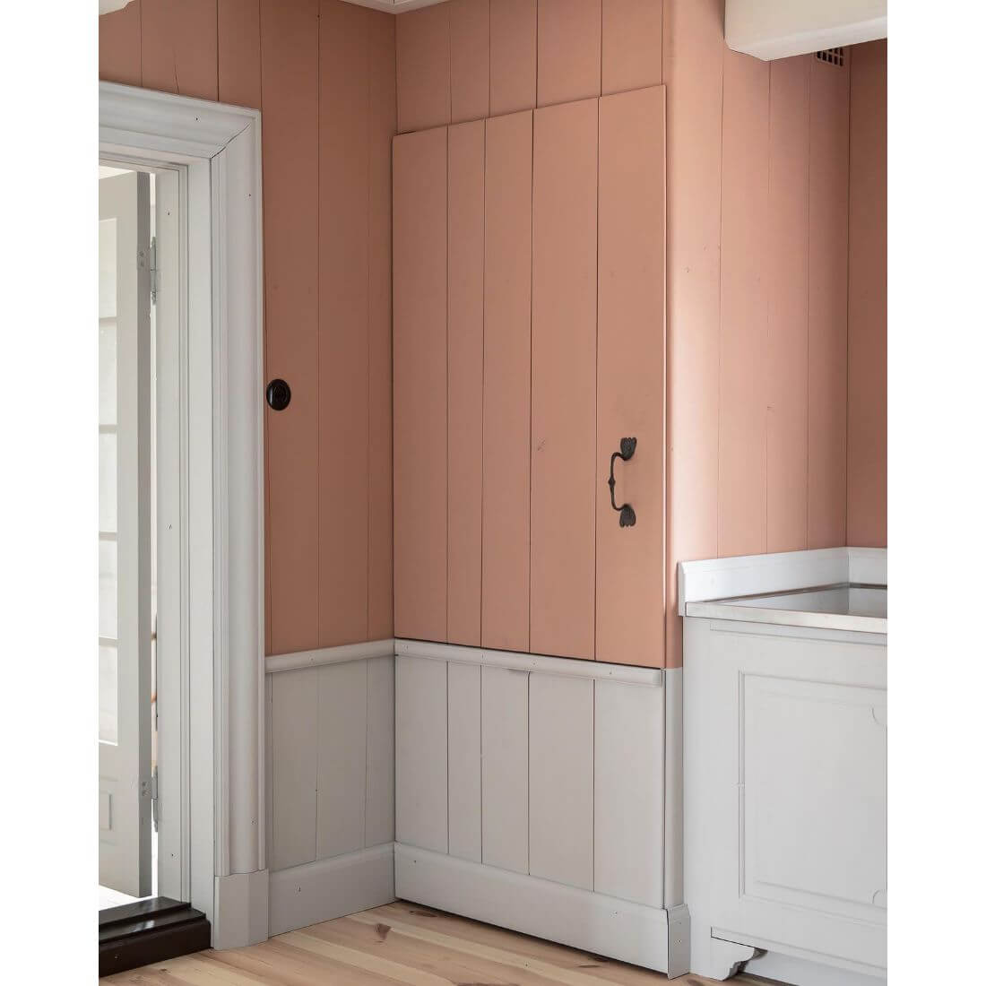 Interior de cozinha com parede rosa e móvel branco, destacando armário embutido.