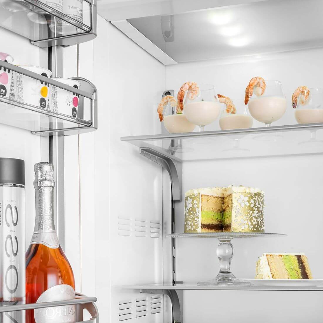 Interior do refrigerador Bertazzoni com sobremesas e bebida espumante, destacando design e organização.