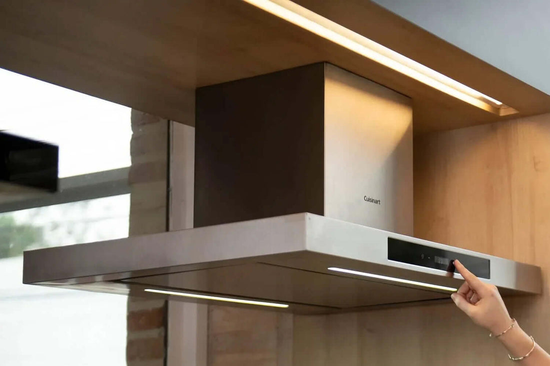 Coifa de parede Cuisinart em aço inox instalada em uma cozinha moderna, com painel digital touch sendo acionado para ajuste de velocidade e iluminação.