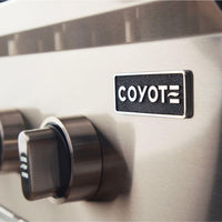 Detalhe do botão e logo da Churrasqueira a Gás Coyote, ressaltando a qualidade do acabamento em aço inox.
