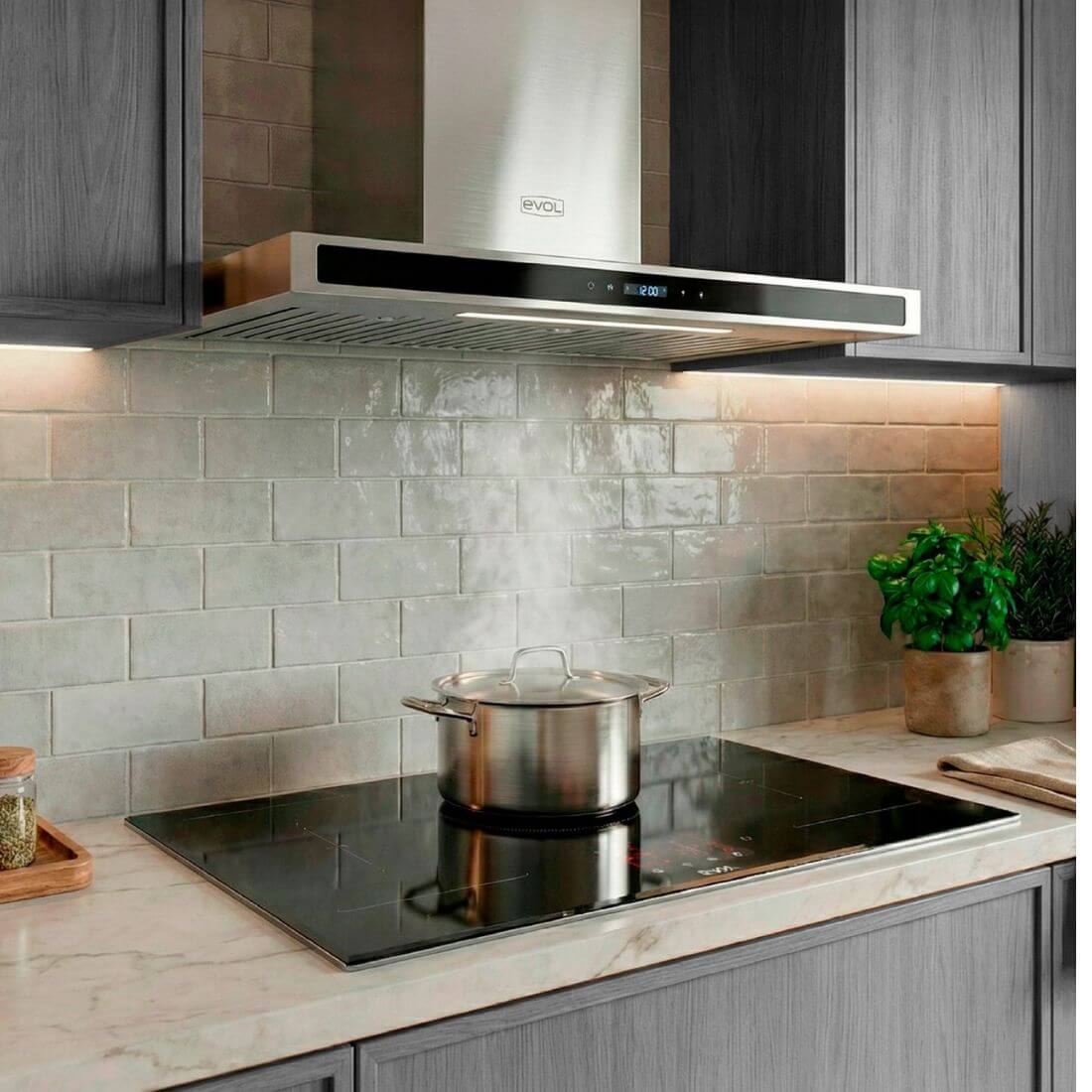 Coifa Evol Sigma de Parede 90cm inox com painel vidro preto instalada sobre cooktop, extraindo vapor de panela e iluminação embutida