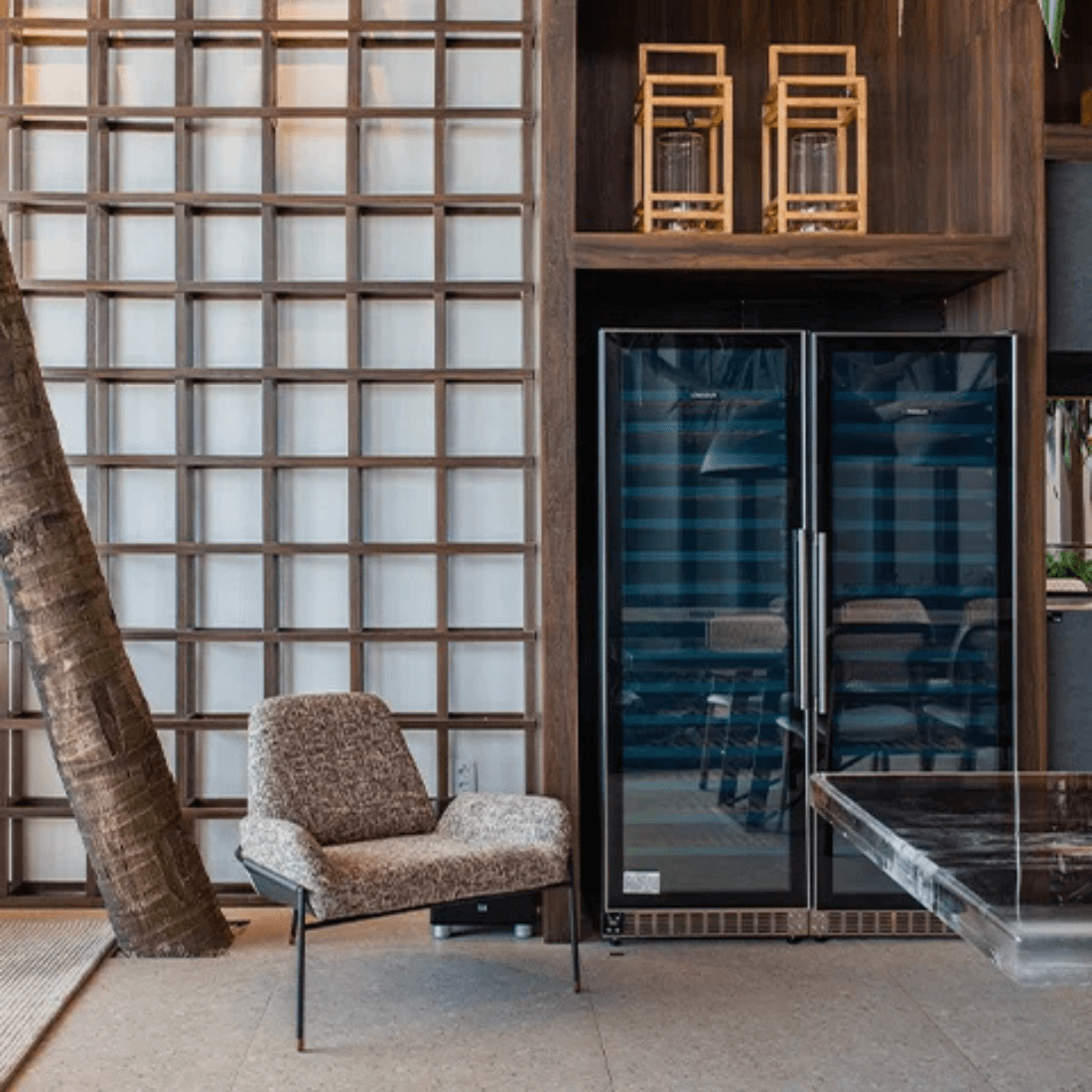 Ambiente moderno com poltrona aconchegante ao lado de uma adega de vinhos em vidro preto.