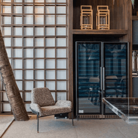 Ambiente moderno com poltrona aconchegante ao lado de uma adega de vinhos em vidro preto.