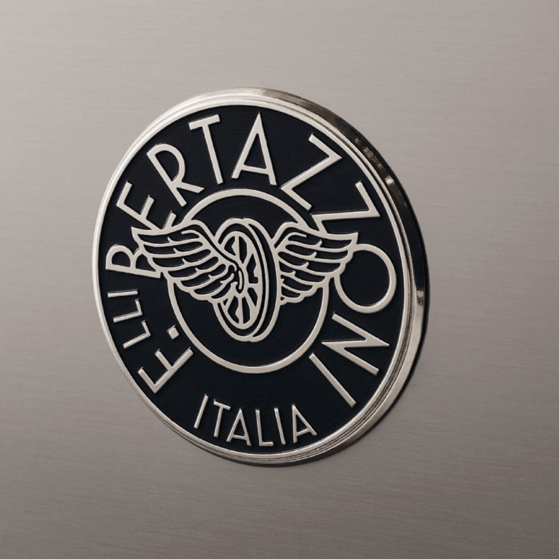Logotipo da Bertazzoni em fundo inox escovado, destacando a tradição italiana de qualidade.