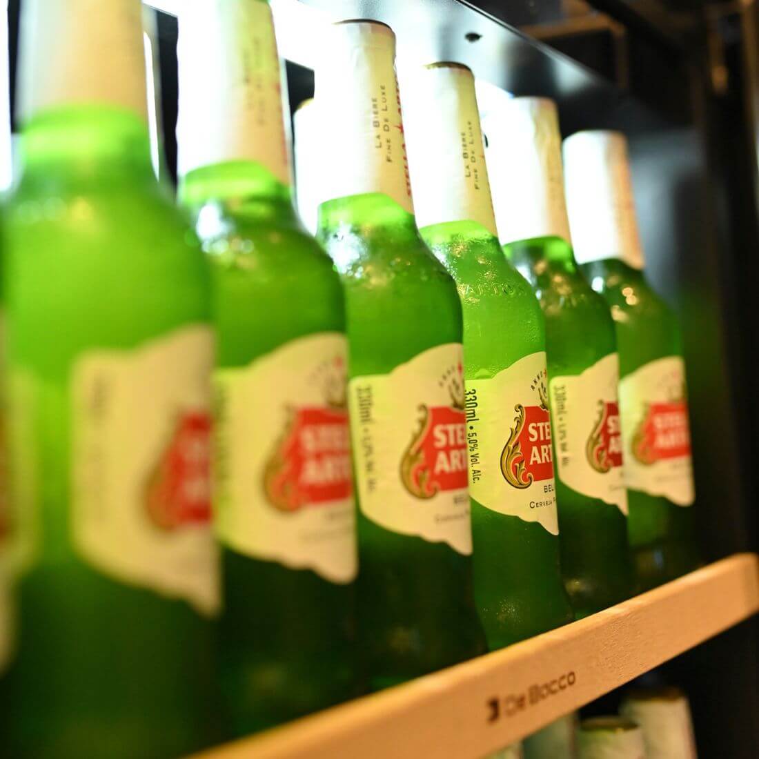 Cervejeira Debacco 145 Litros Inox 60cm - Abertura Esquerda mostrando prateleiras em metal aramado com garrafas, acabamento inox e porta de vidro