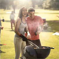 Churrasqueira a Carvão Weber Original Kettle: casal feliz grelhando em parque com churrasqueira preta, tampa, pegador e fumaça no convívio ao ar livre