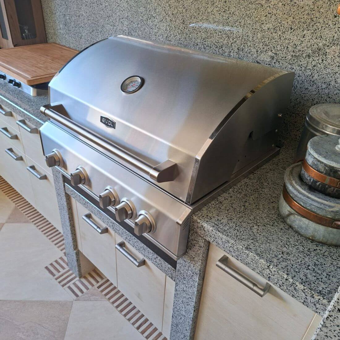 Churrasqueira a Gás Evol Florence 4 Queimadores Inox 79cm instalada em bancada de granito com tampa inox, puxador e quatro botões frontais
