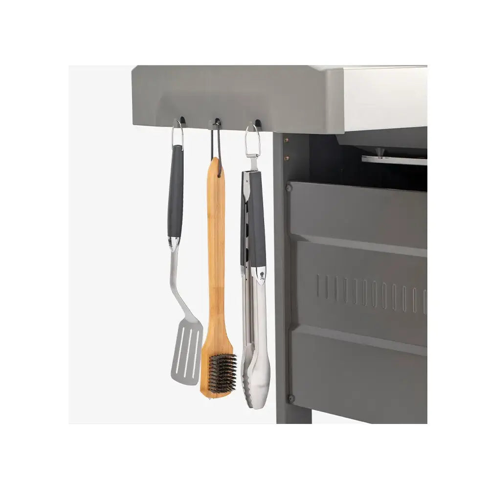 Churrasqueira a Gás Weber 3 Queimadores 130 cm com Rodízio Gênesis II E-335 exibindo gancho lateral com espátula, pegador e escova em inox e madeira