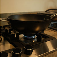 Cooktop à Gás Debacco Zurique 5 Bocas Inox 70cm mostrando queimador aceso com panela wok, trempes em ferro e acabamento inox escovado