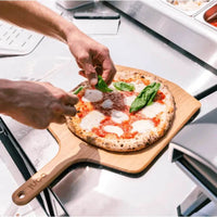 Espátula e Tábua de Bambu Ooni com pizza sendo servida, destacando seu uso prático e elegante.