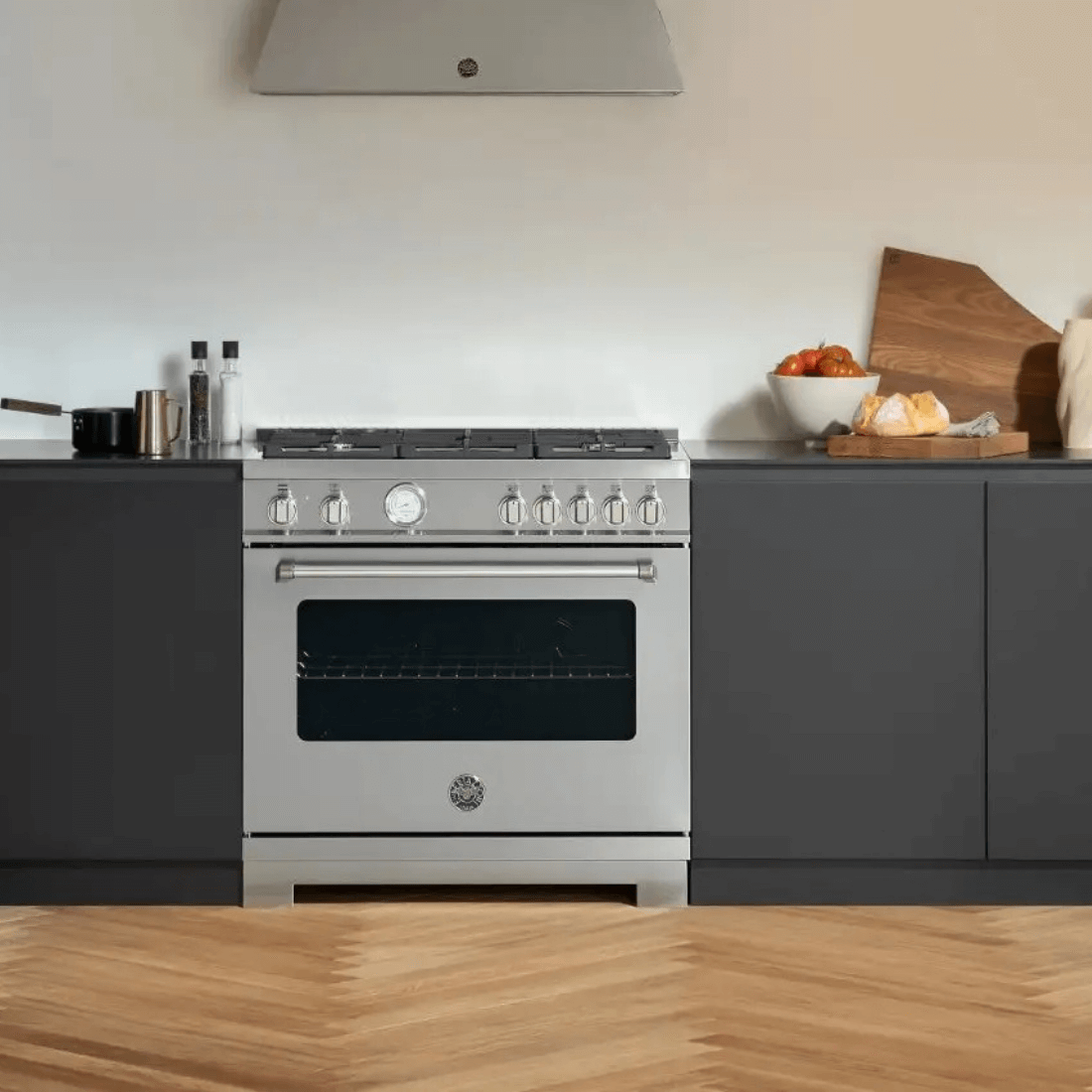 Fogão Bertazzoni Master 5 bocas em inox na cozinha moderna com armários escuros e bancada de madeira.