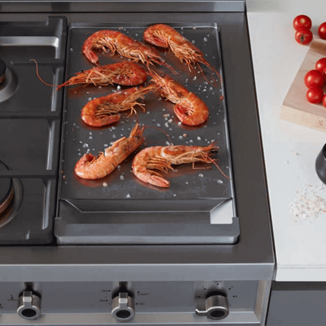 Camarões grelhados em chapa sobre fogão Bertazzoni, com queimadores a gás e detalhes em inox.