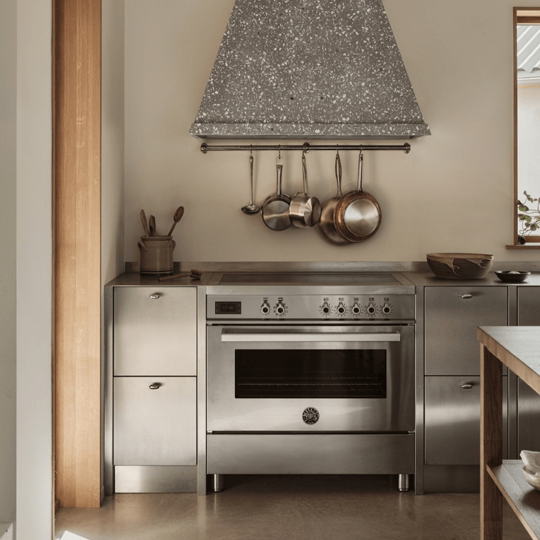 Fogão Bertazzoni profissional em inox na cozinha moderna com bancada e utensílios de cozinha.