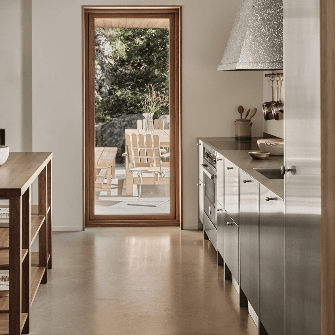 Cozinha moderna com fogão inox, mesa de madeira e vista para o exterior iluminado.