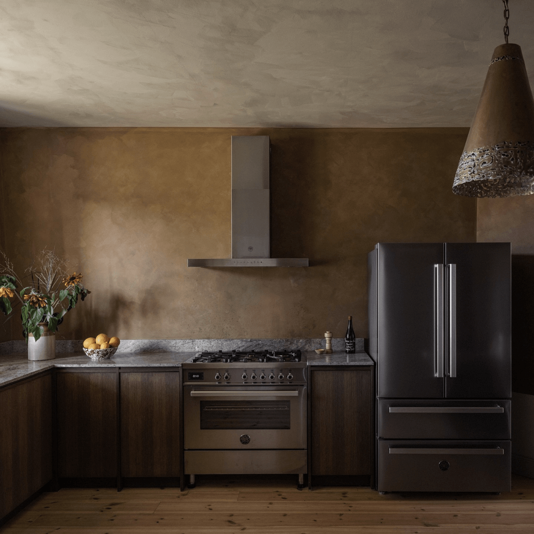 Cozinha moderna com fogão inox, geladeira escura e decoração em tons terrosos.