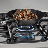 Wok com cogumelos e pimentas cozinhando em fogão Lofra, com chamas azuis visíveis.