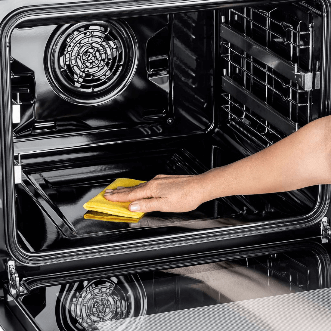 Forno Tecno Original Elétrico 72 Litros Inox 60cm sendo limpo por dentro, acabamento inox, porta de vidro e ventilador traseiro visíveis