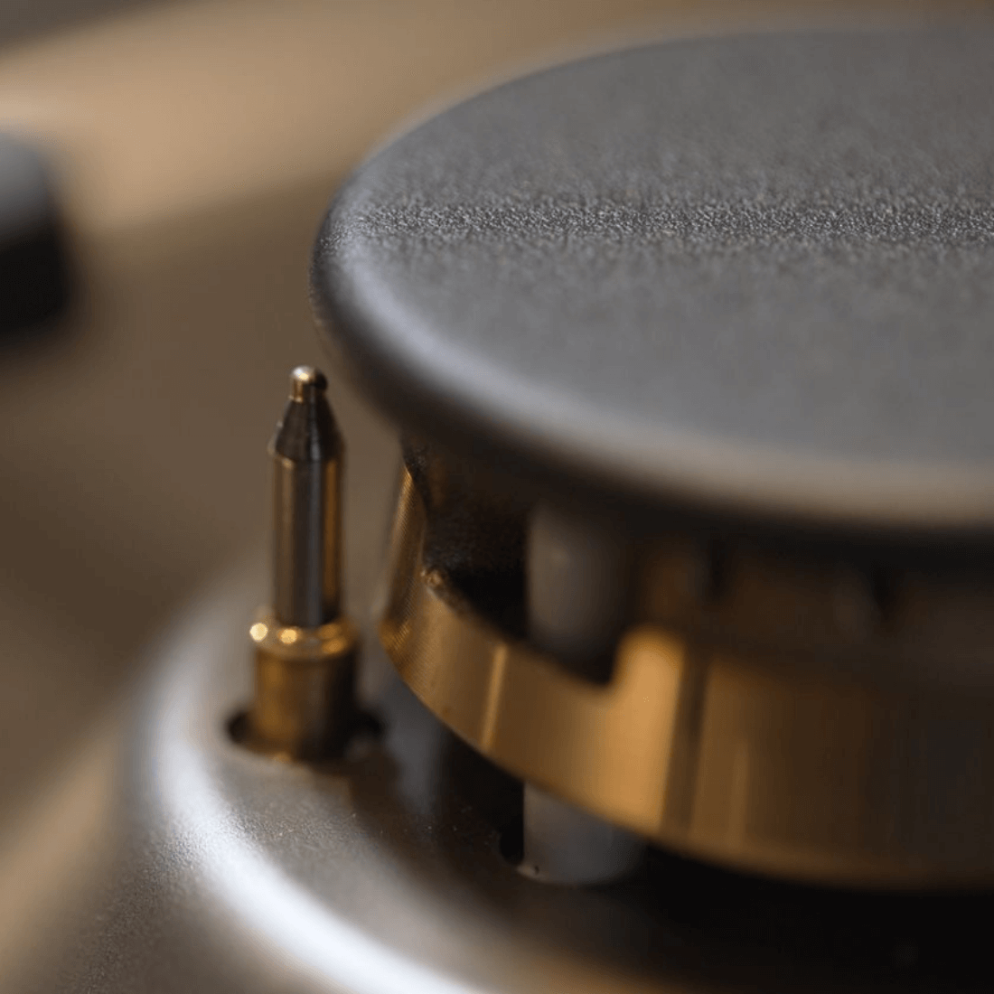 Detalhe de queimador de fogão Bertazzoni com botão de acendimento automático em inox e acabamento em dourado.