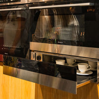 Gaveta Aquecida Debacco Montreal Inox e Vidro 60cm em inox com frente de vidro, puxador discreto e instalação de embutir mostrando xícaras aquecidas