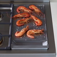 Camarões grelhados em um suporte de panela wok, em destaque na RangeTop Bertazzoni Master 6 bocas a Gás e Grill Elétrico Inox 122cm.